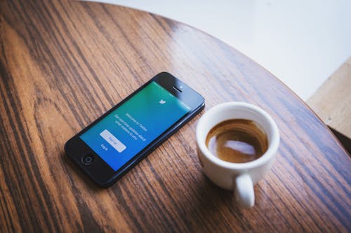 White Ceramic Teacup Beside Black Iphone 5 on Brown Wooden Table