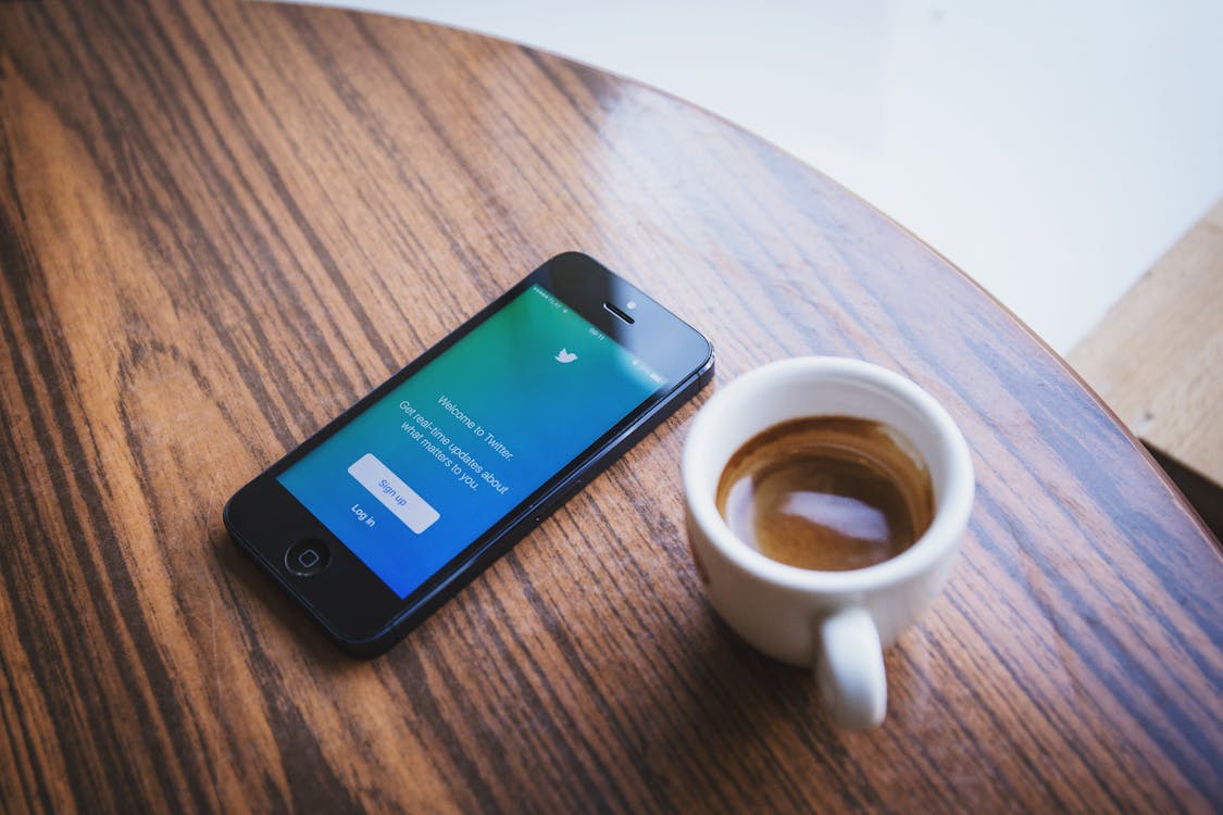 White Ceramic Teacup Beside Black Iphone 5 on Brown Wooden Table