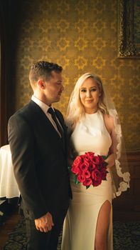 身着正式西装的新郎和穿着白色婚纱、头戴面纱、手持一束鲜艳红玫瑰的新娘，洋溢着幸福