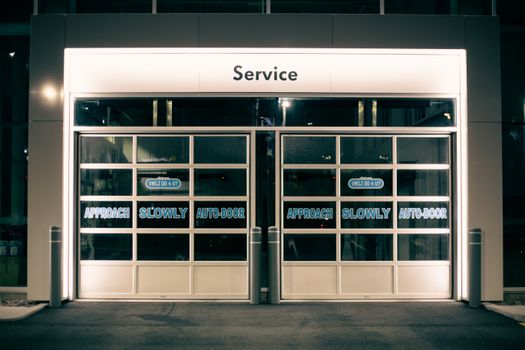 Modern glass service entrance illuminated at night with automatic doors.