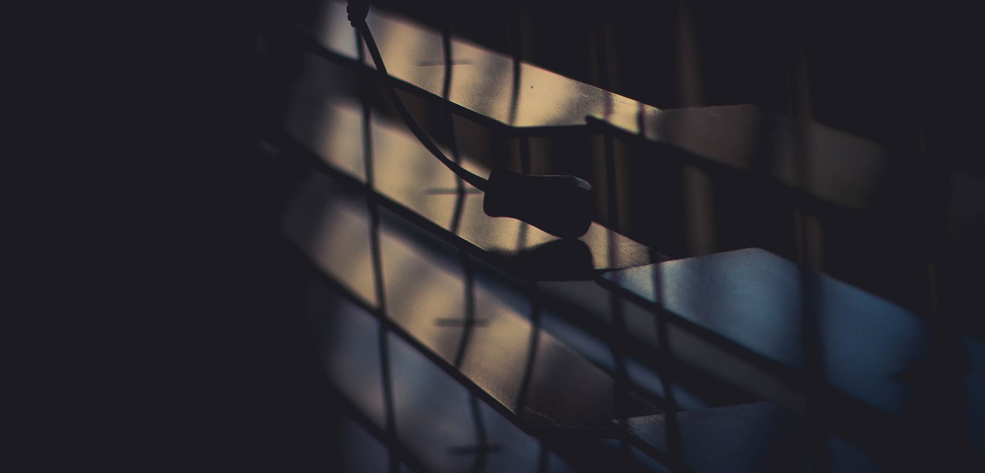 A dramatic close-up of window blinds casting a silhouette in soft lighting.