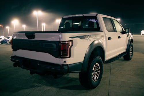 White pickup truck on parking lot with cars under shiny streetlamps at night