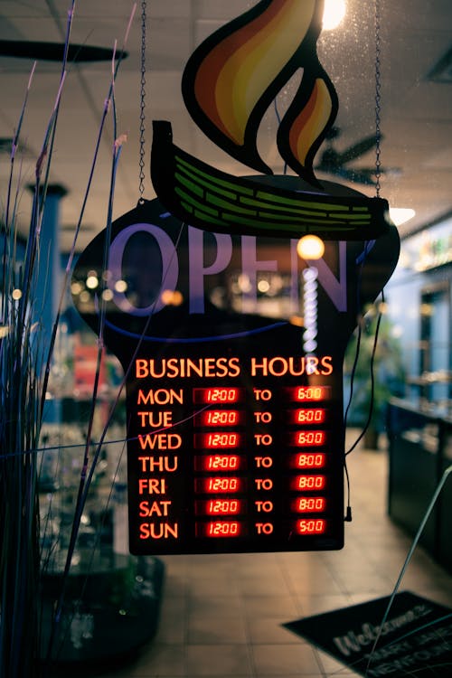Through glass of information board with glowing business hours hanging on glass door at entrance of cafe
