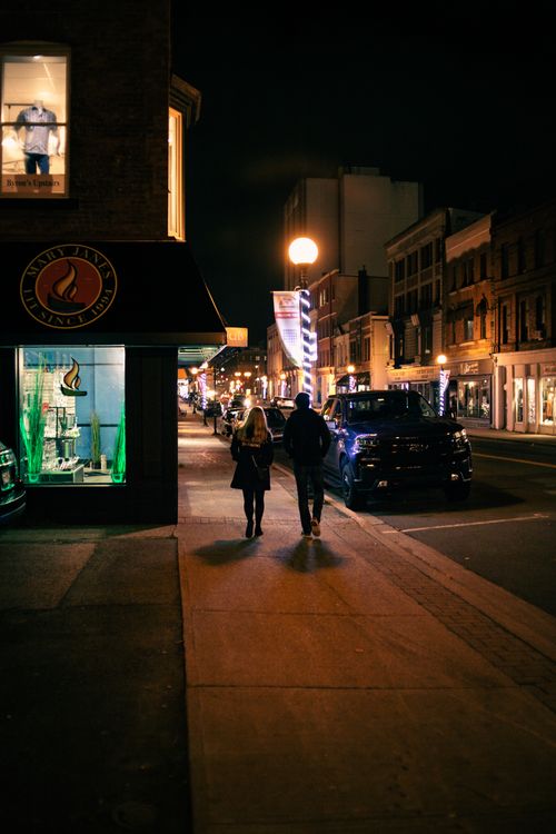 Free Full body back view of anonymous couple strolling on pavement near buildings and road with parked cars at night Stock Photo