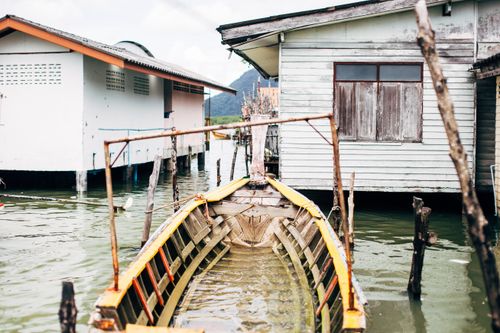 Free A serene view of a wooden boat moored next to rustic lakeside houses on a clear day. Stock Photo
