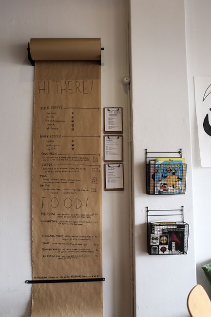 Kraft paper roll menu on cafe wall with handwritten food and drink items next to wire wall organizers with clipboards