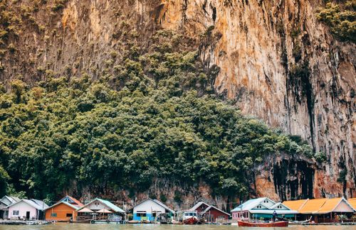 Free Colorful floating houses against a lush, rocky limestone backdrop on a serene lake. Stock Photo