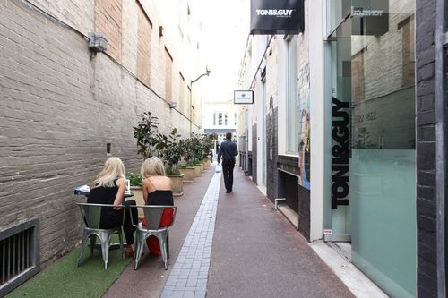 Free Discover a serene alley café setting with people enjoying a leisurely day. Urban vibe with eateries and shops. Stock Photo