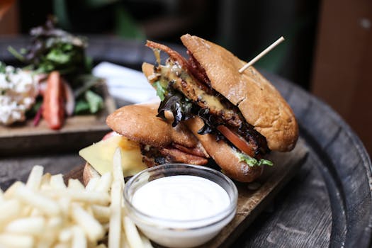 Close-up of a gourmet burger with fries, side salad, and dipping sauce in a rustic restaurant setting.