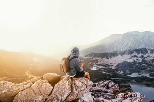 Free A lone traveler with a backpack sitting on a mountain rock, enjoying the scenic sunrise view. Stock Photo