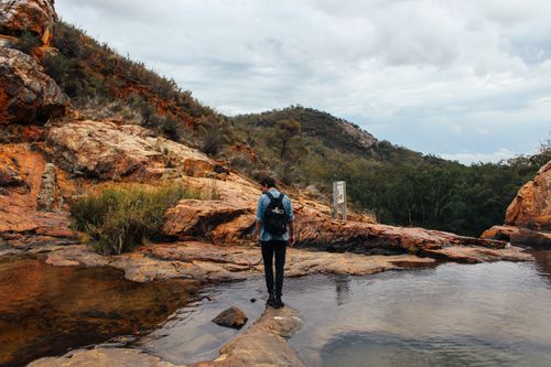 Free A man stands near a rocky river in a mountainous landscape, exploring nature. Stock Photo