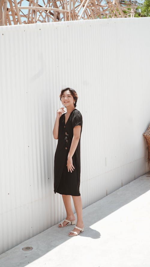 Woman in Black Dress Standing on Concrete Pavement Near White Wall