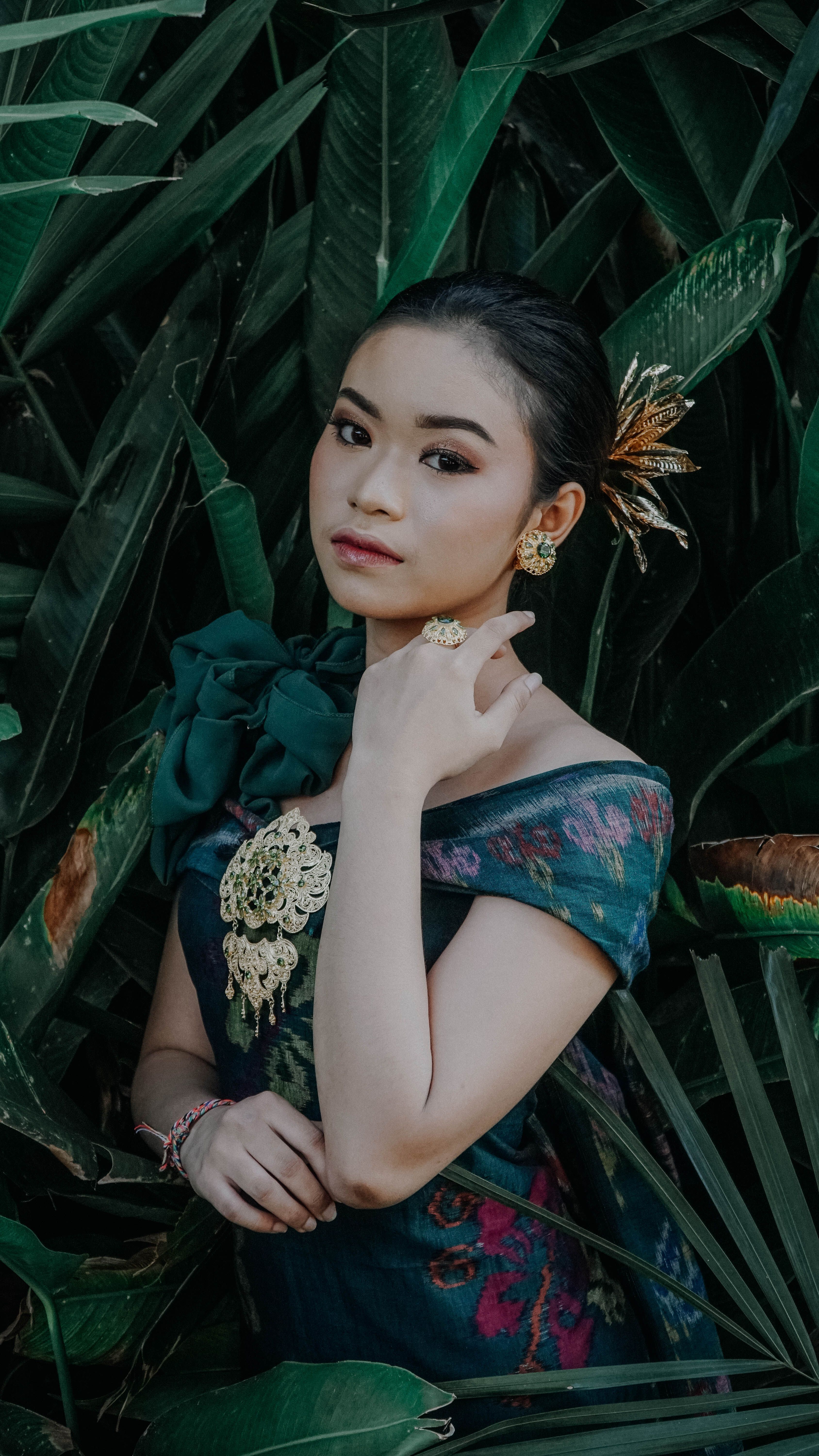Beautiful Indonesian woman in traditional dress amidst lush green leaves in Bali.