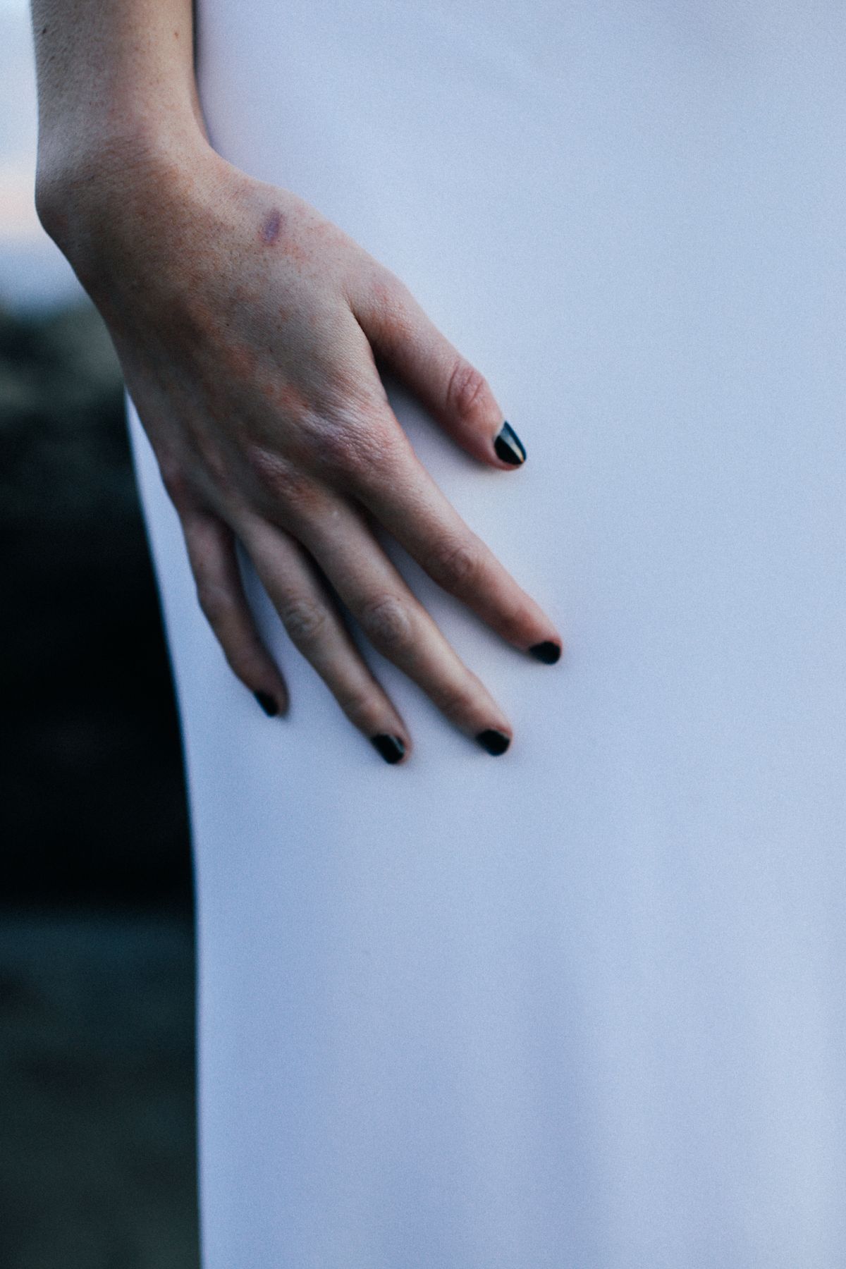 Elegant hand with dark nail polish resting on a white garment, evoking minimalism.
