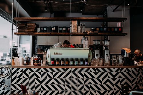 Free Modern coffee shop interior featuring a stylish counter with geometric patterns and shelves with cups and coffee bags. Stock Photo