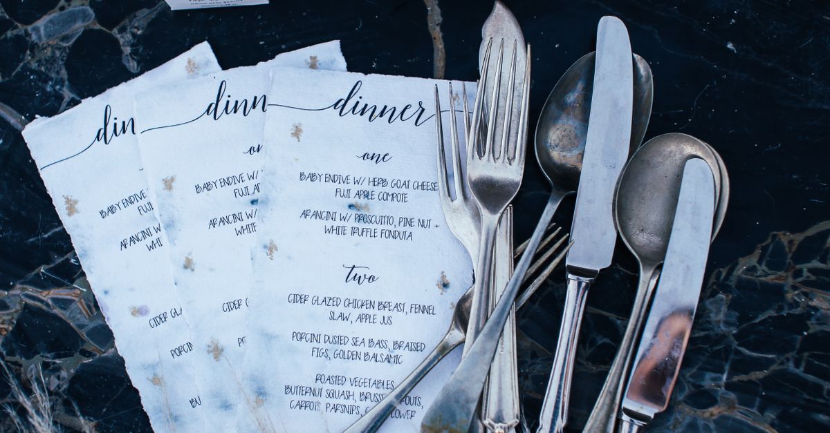 Stylish dinner menus with classic silver cutlery on a patterned marble surface, exuding a vintage vibe.