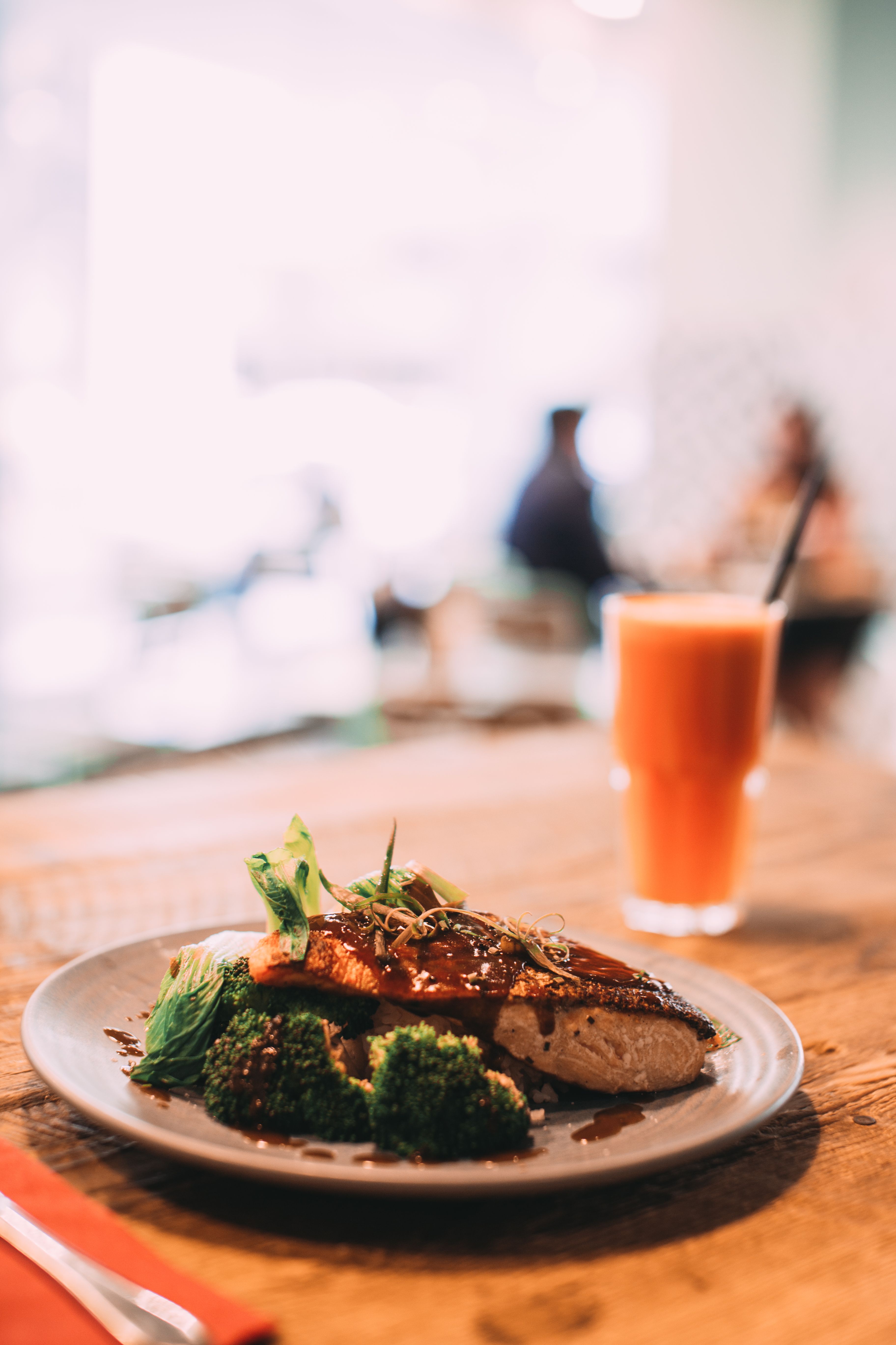A tantalizing salmon dish served with broccoli and carrot juice on a wooden table in a restaurant setting.