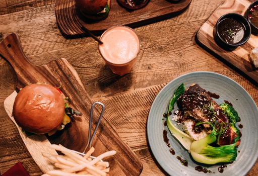 Top view of a meal with gourmet burger, stir fry dish, and a smoothie on a rustic table.