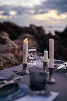 Elegant outdoor dinner setting with candles and tableware at sunset, creating a warm, romantic ambiance.
