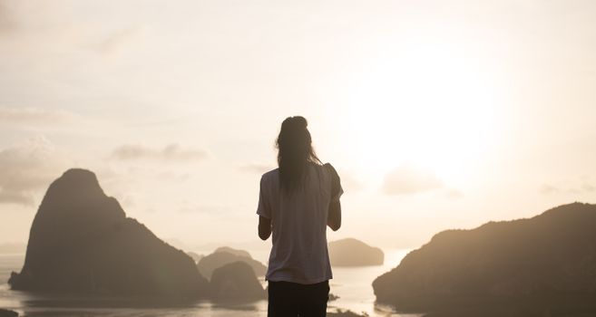 日出时分，一名女子站在悬崖上，俯瞰着雾气缭绕的岛屿与海洋，画面传递出宁静与奇迹之感