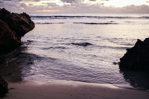 A tranquil seashore scene at dusk with gentle waves and rocky boulders.