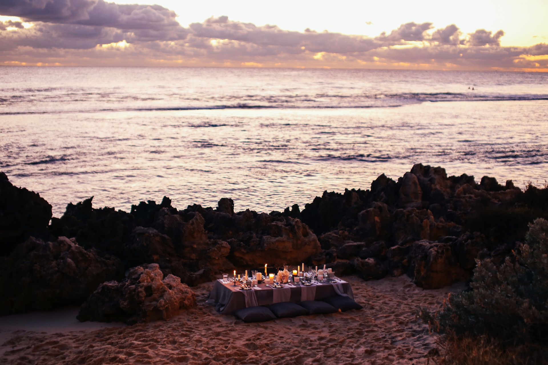 Beautifully arranged seaside dinner setup with candles at sunset, perfect for a memorable evening.