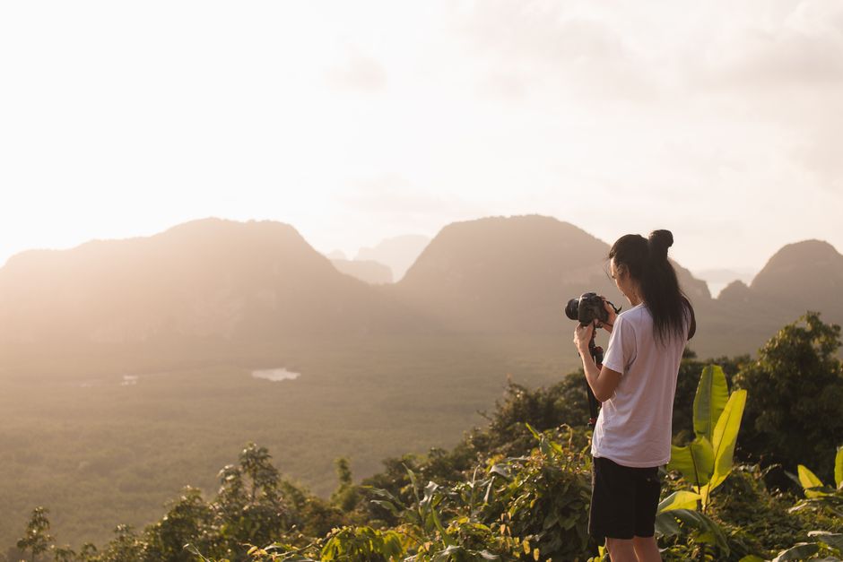 A person with a camera takes photos of a stunning mountain landscape at sunset. Perfect for travel and nature themes.