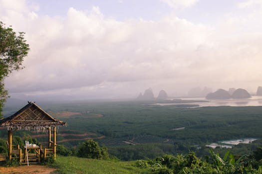 Tranquil countryside scene featuring a nipa hut overlooking lush greenery and distant hills under a hazy sky.