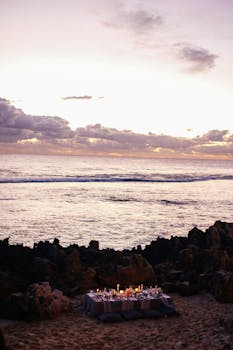 Serene beachfront setup with candles and ocean view at sunset, perfect for romantic occasions.