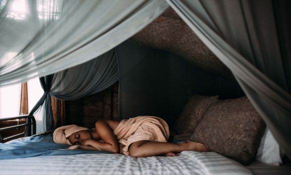 一位女士安静地躺在铺着透明天篷窗帘的舒适床上，营造出宁静的室内静修氛围
