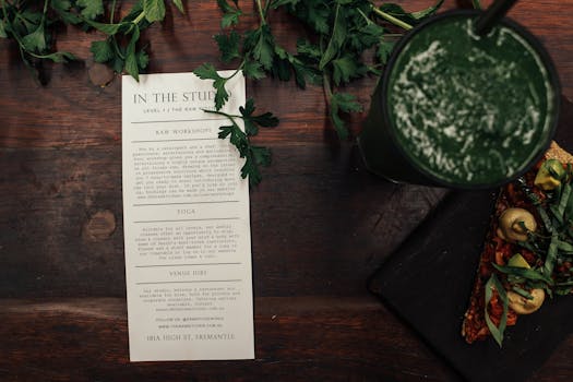 Top view of green smoothie, workshop flyer, and healthy flatbread on a wooden table.