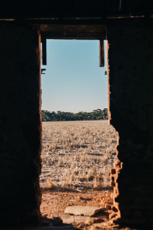 Free A rustic, aged doorway frames a view of a vast, arid landscape under a clear blue sky. Stock Photo