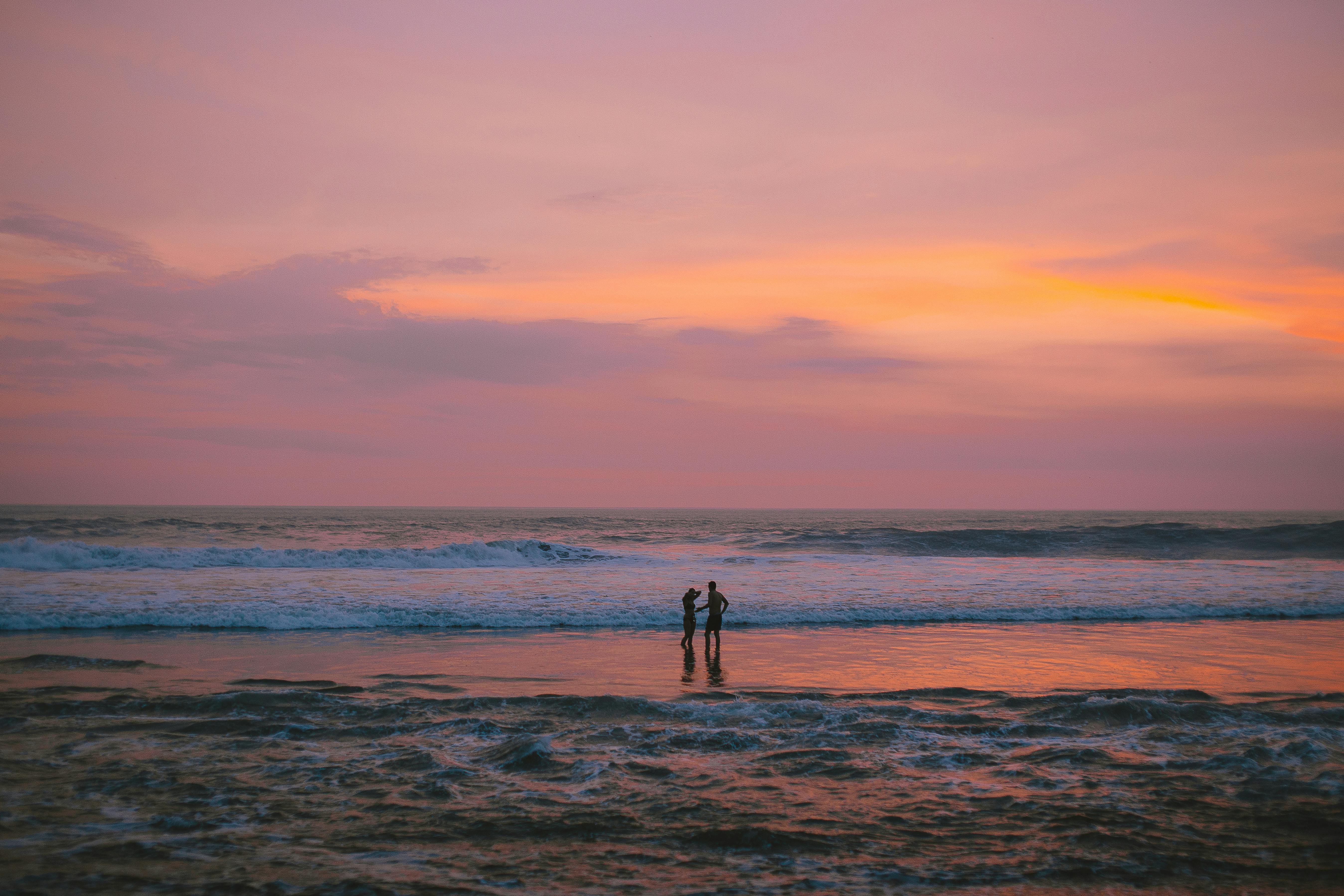 一对夫妇在令人惊叹的日落天空下，沿着海滩平静地散步