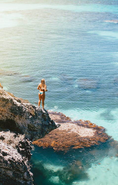 A Woman in Bikini Standing on Rock Formation Near Body of Water · Free ...