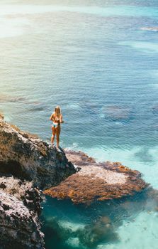Woman in bikini on a cliff edge looking at the ocean, capturing a summer vibe.