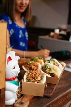 Close-up of Asian street food in boxes on wooden tray with a blurred background in vibrant setting.