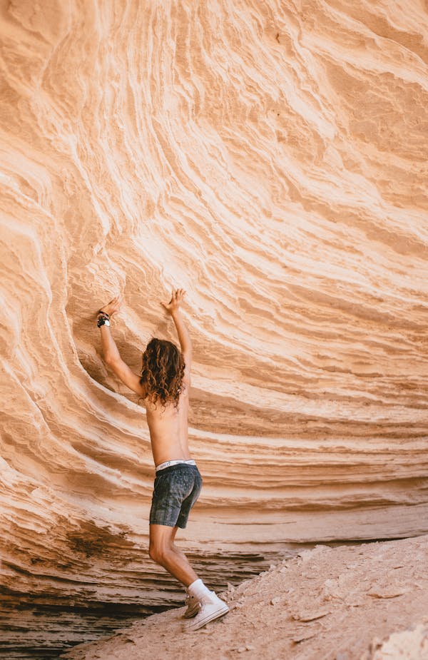 Man in Black Shorts Touching a Rock Formation
