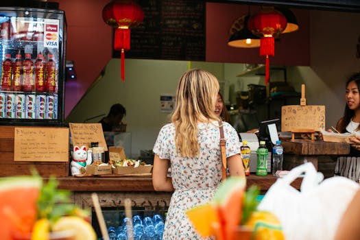 Woman in floral dress ordering at a snack bar with Asian decor and light refreshments visible.