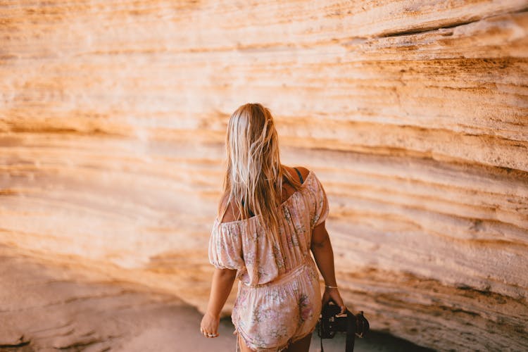 Woman Wearing A Floral Romper Holding A Camera Near Rock Wall