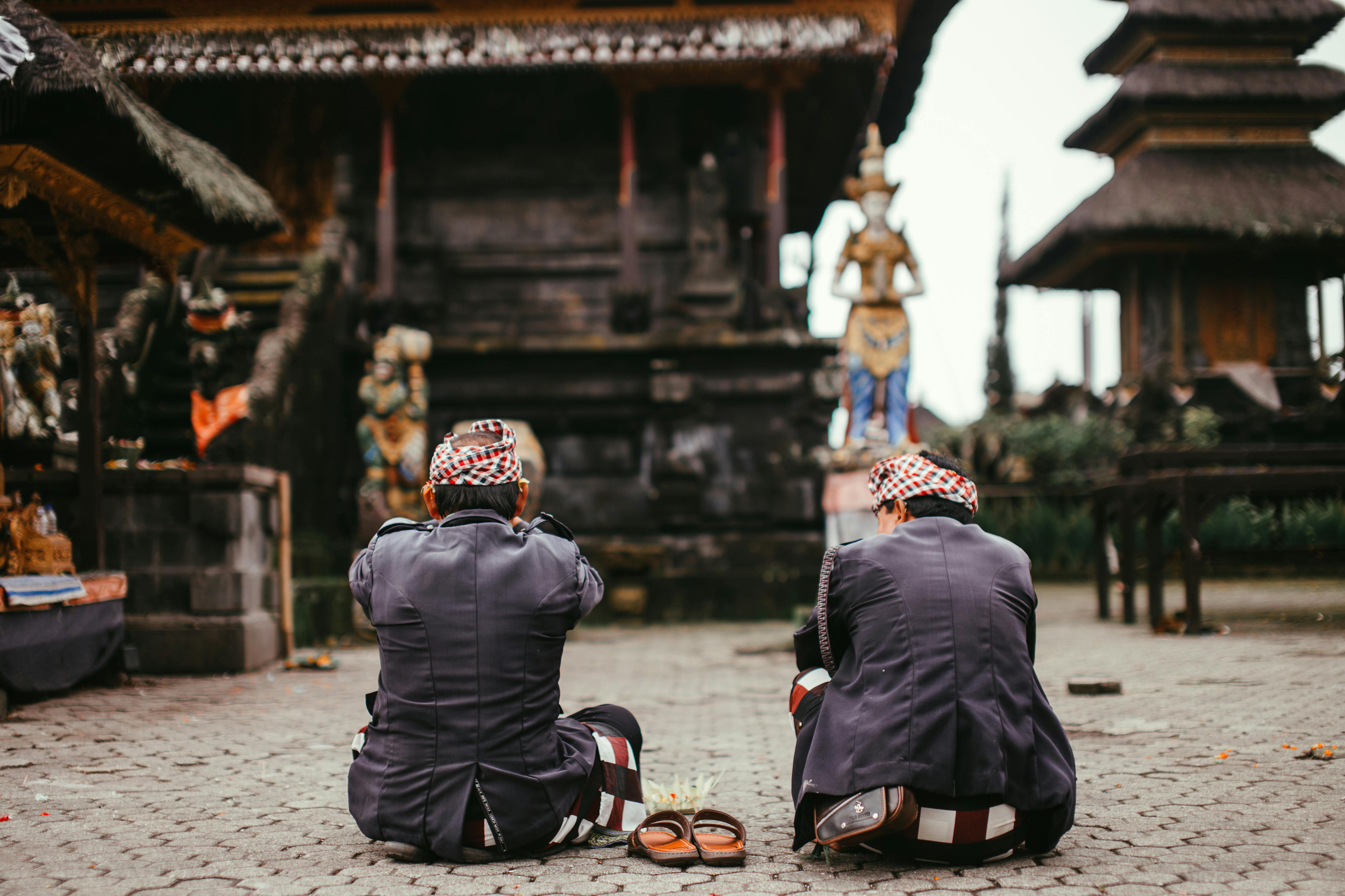 Two people praying outdoors at a traditional Balinese temple.