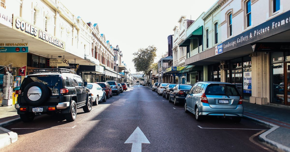Vibrant city street with parked cars and local shops on a sunny day.
