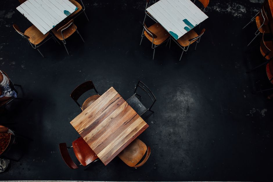 Aerial shot of rustic wooden tables and chairs in a dimly lit restaurant setting.