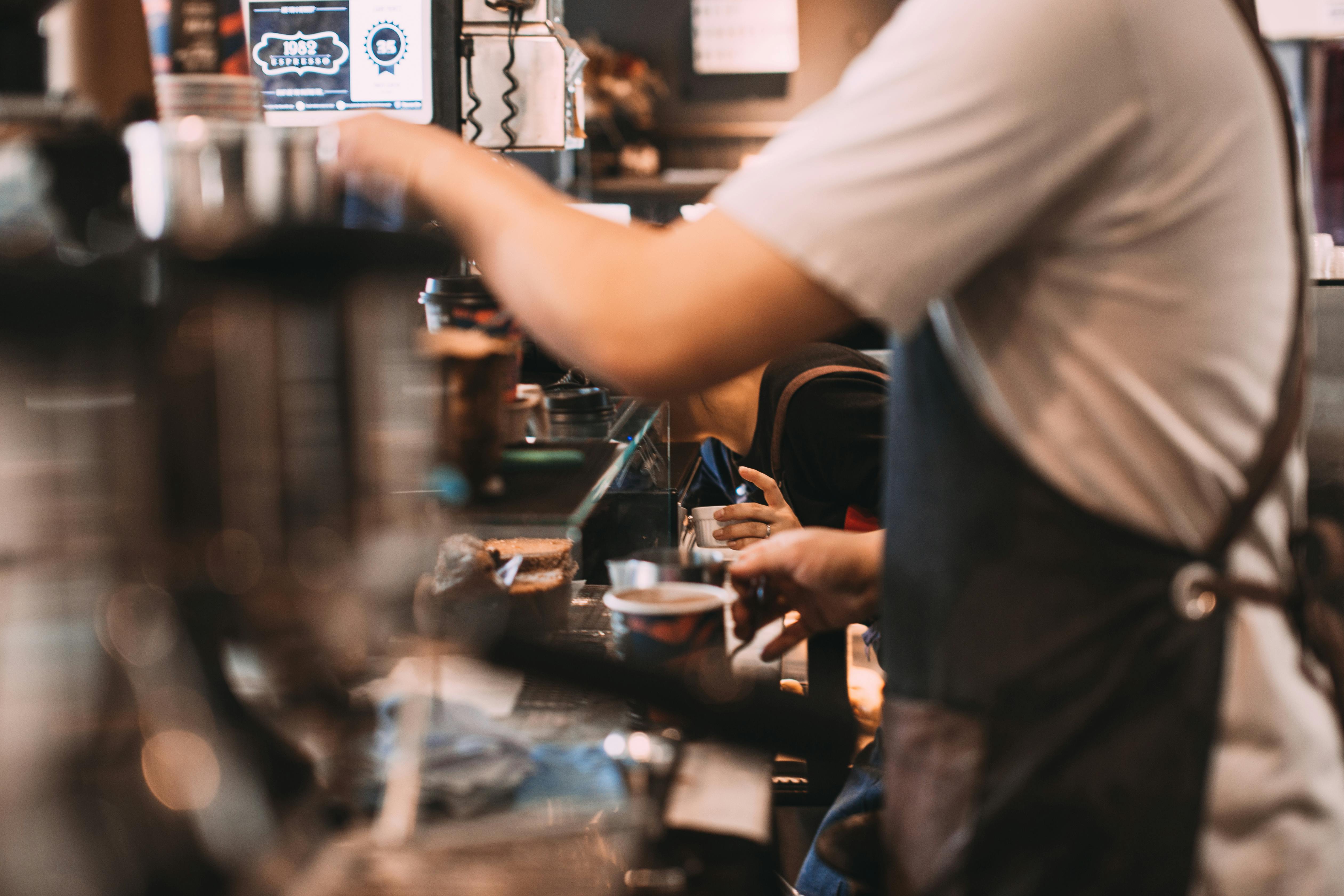 A barista skillfully prepares coffee at a busy café counter, showcasing expert technique.