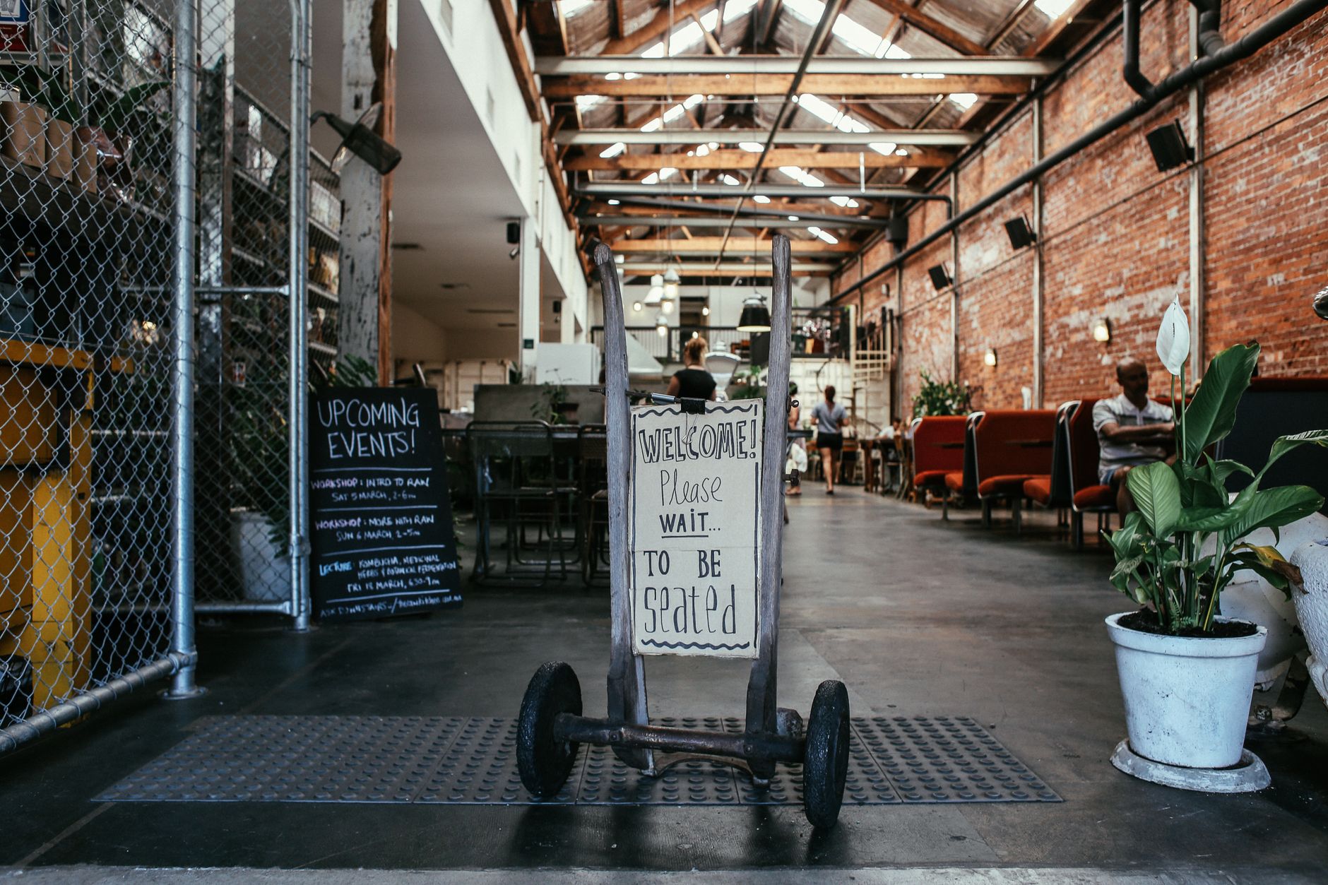 Industrial-style restaurant interior with seating sign and vibrant plants.