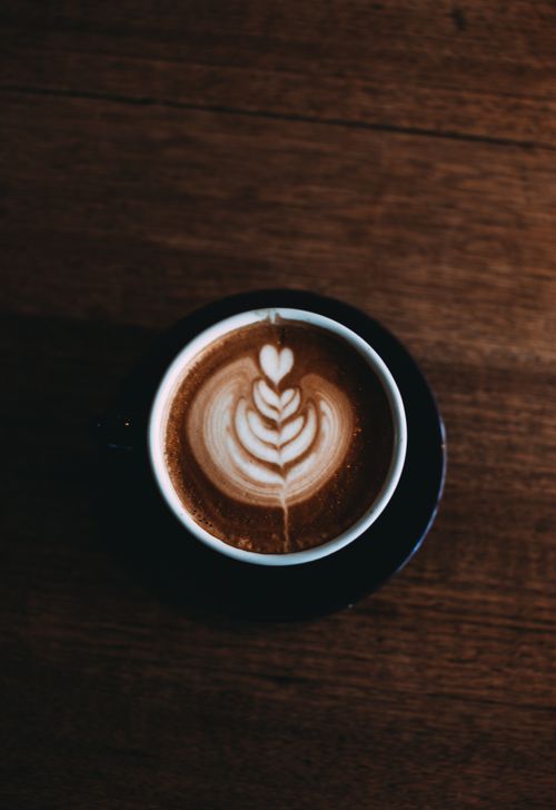 Free A top view of a cappuccino cup with intricate latte art sitting on a rustic wooden table. Stock Photo