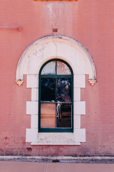 A classic arched window with reflection on a rustic pink wall, offering architectural charm.
