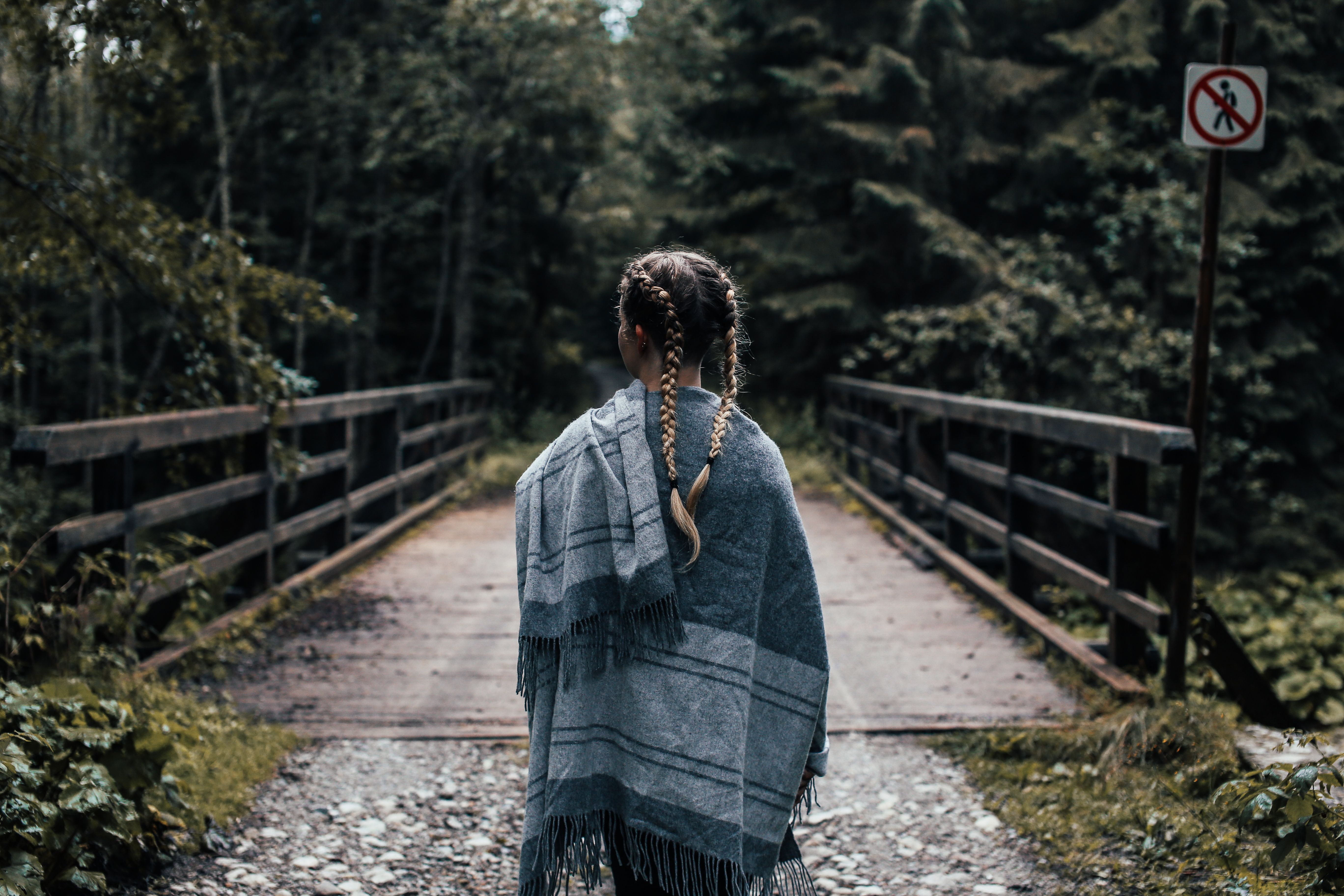 一名扎着辫子的妇女裹着披肩，站在森林中郁郁葱葱的桥上