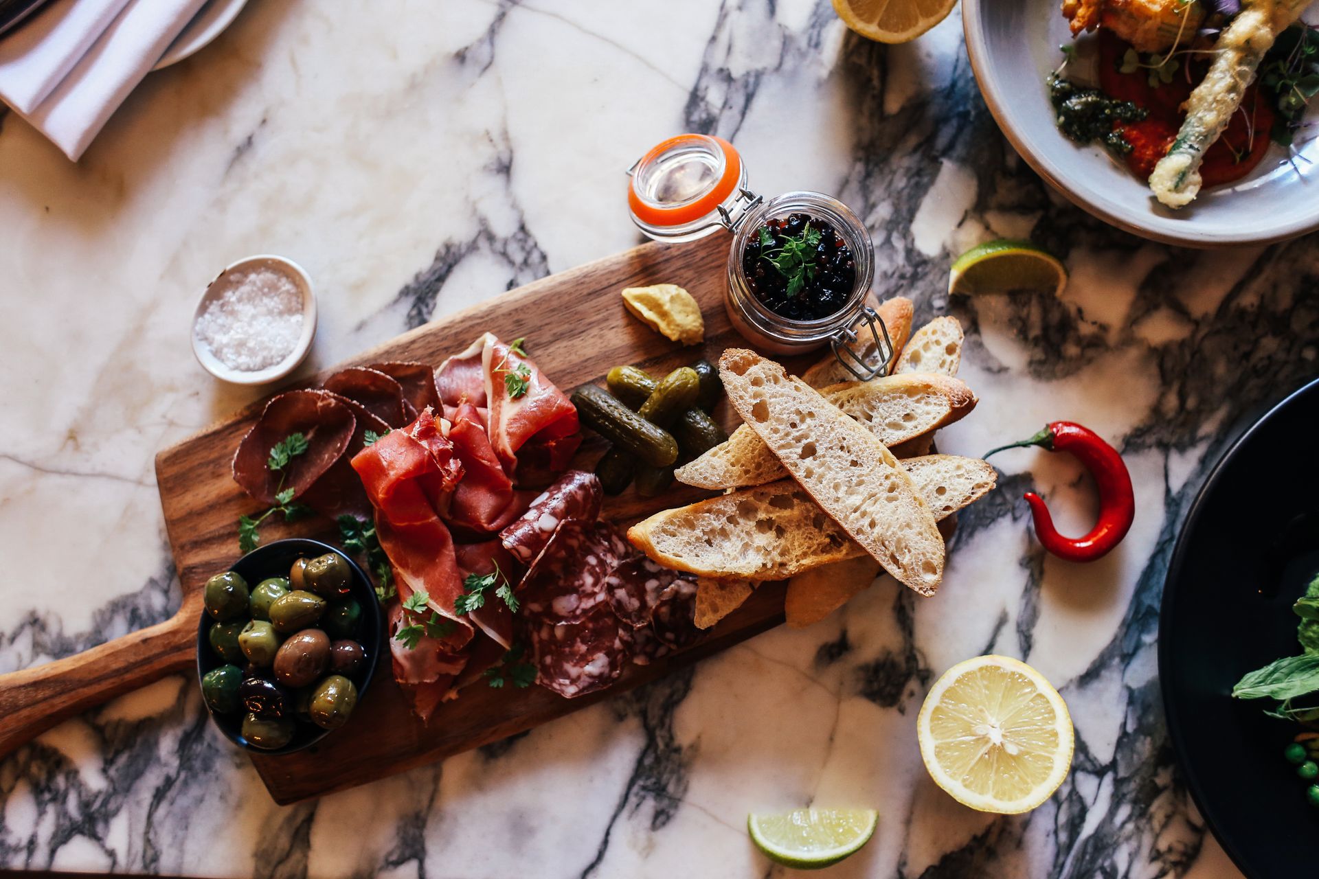 A rustic charcuterie board with meats, olives, and bread on a marble table.