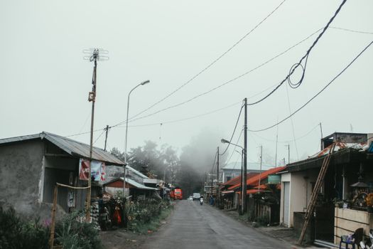 雾气弥漫的村庄街景中，电缆和路灯在多云的天空下若隐若现