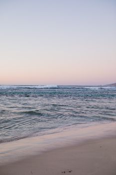 日落时分，海滩景色宁静，海浪轻柔，天空柔和